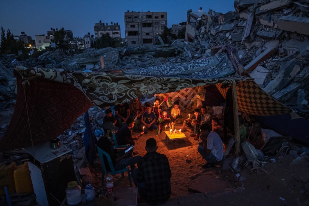 des enfants palestiniens tiennent des bougies lors d’un rassemblement au milieu des ruines des maisons détruites par les frappes israéliennes