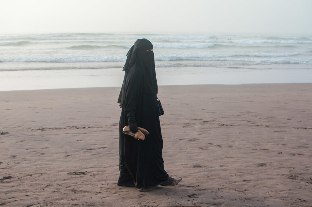 Jeune femme en burqa, marchant seule sur le sable, à la plage. Casablanca, septembre 2016.